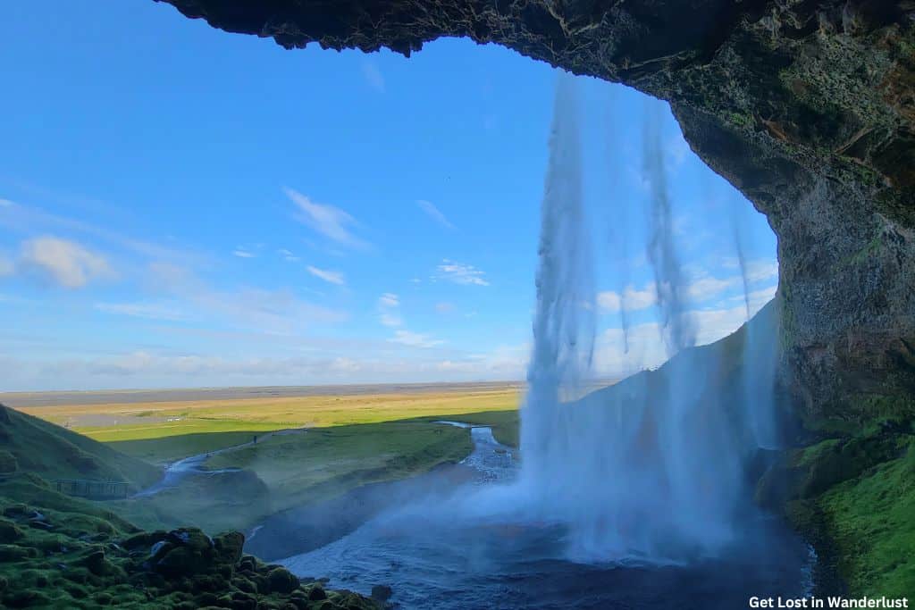 View of water cascading down Seljalandsfoss, and surrounding green scenery.