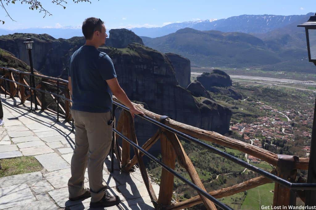 Man looking out over the Meteora view point edge to the town and surrounding mountains.