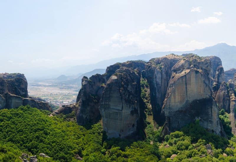 View of the Meteora rock formations with lush green trees below.