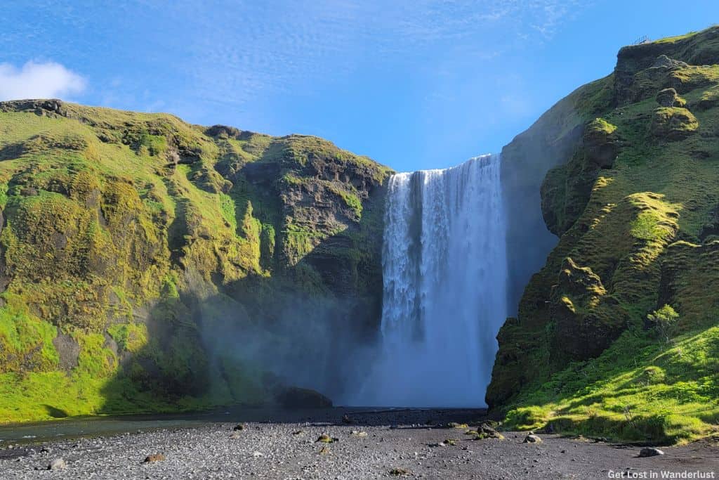 Skogafoss, an impressively wide waterfalls surrounded by green moss covered cliffs.