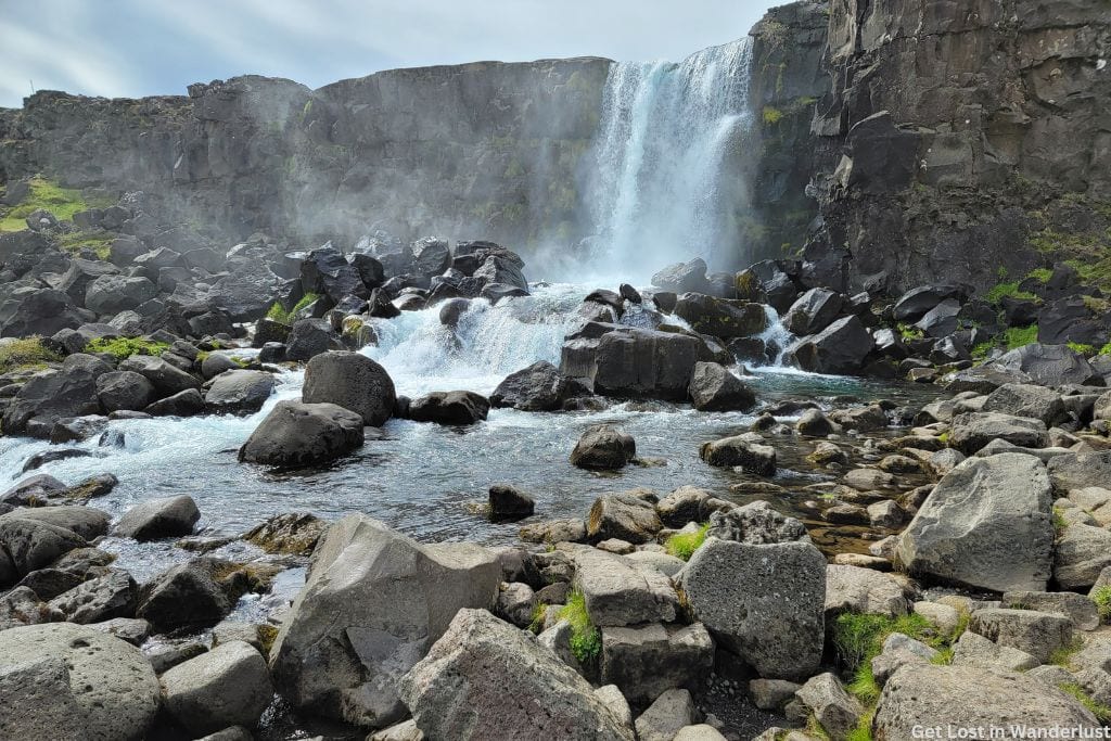 Small waterfall surrounded by rocky cliffs and large gray rocks at the bottom.
