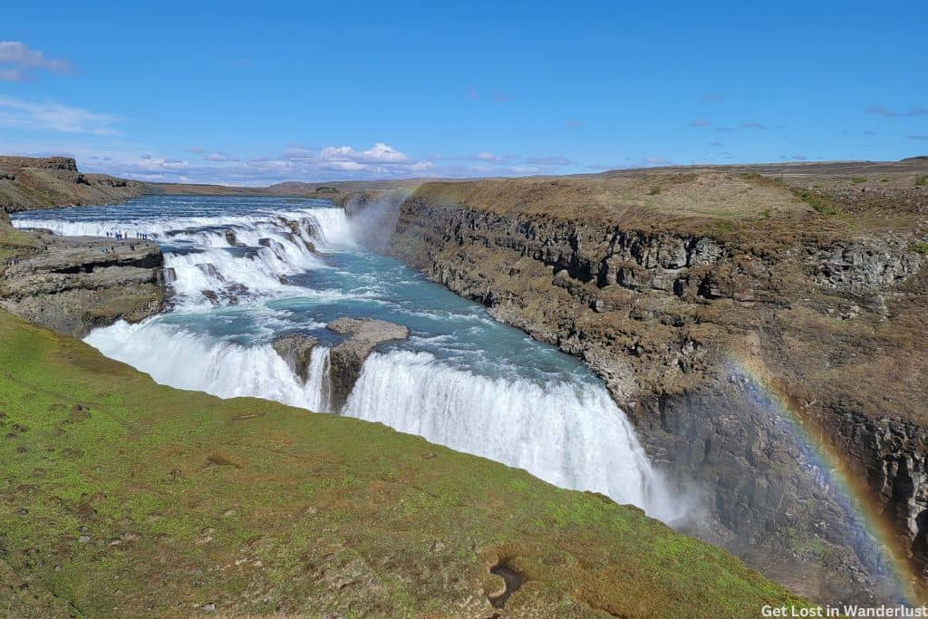 The double waterfall of Gullfoss, with a slight rainbow in the corner. In the background is the green landscape.