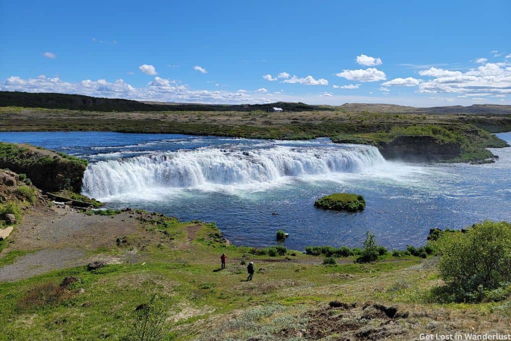 Green landscape around the large Tungufljót River. In the center is the Faxi waterfall, with water flowing quickly over the falls.