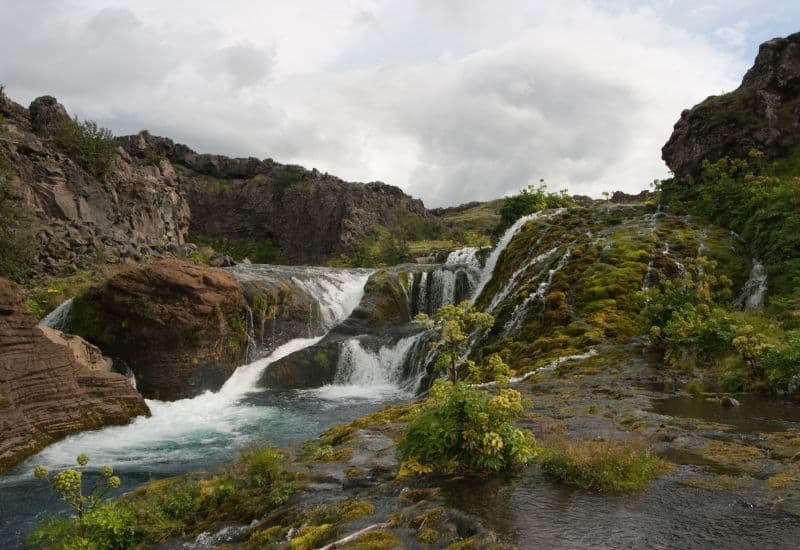 Cascading waters of Gjáin Waterfall going into a pool of water, surrounded by a green moss covered valley.