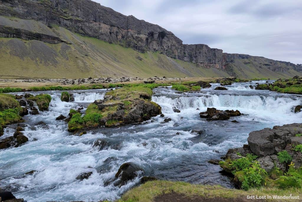 Fossálar Waterfall, a small waterfall with several levels feeding into a large river.