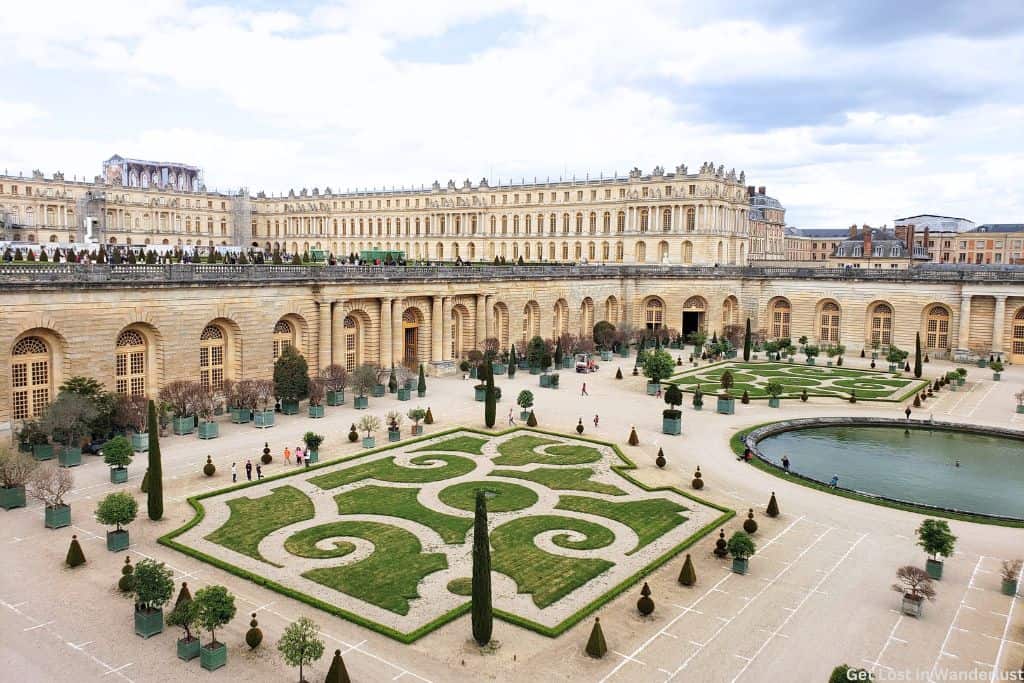The exterior of the Palace of Versailles with some of the beautifully manicured gardens in the front.