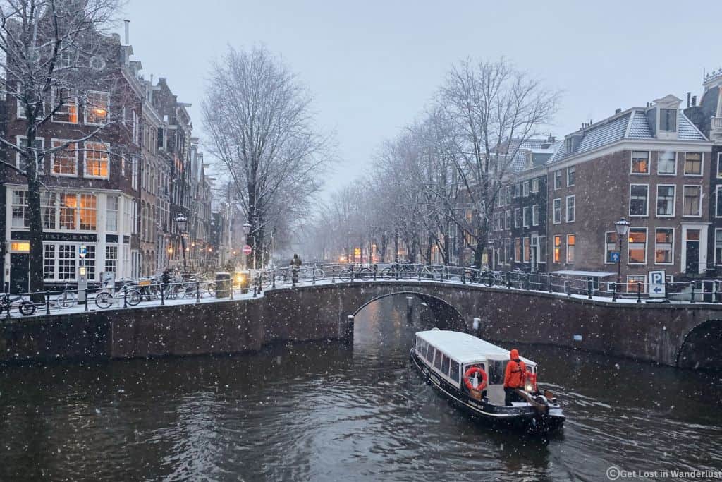 A canal cruise going through the Amsterdam canals on a snowy day in January, with the picturesque canal houses in the background.