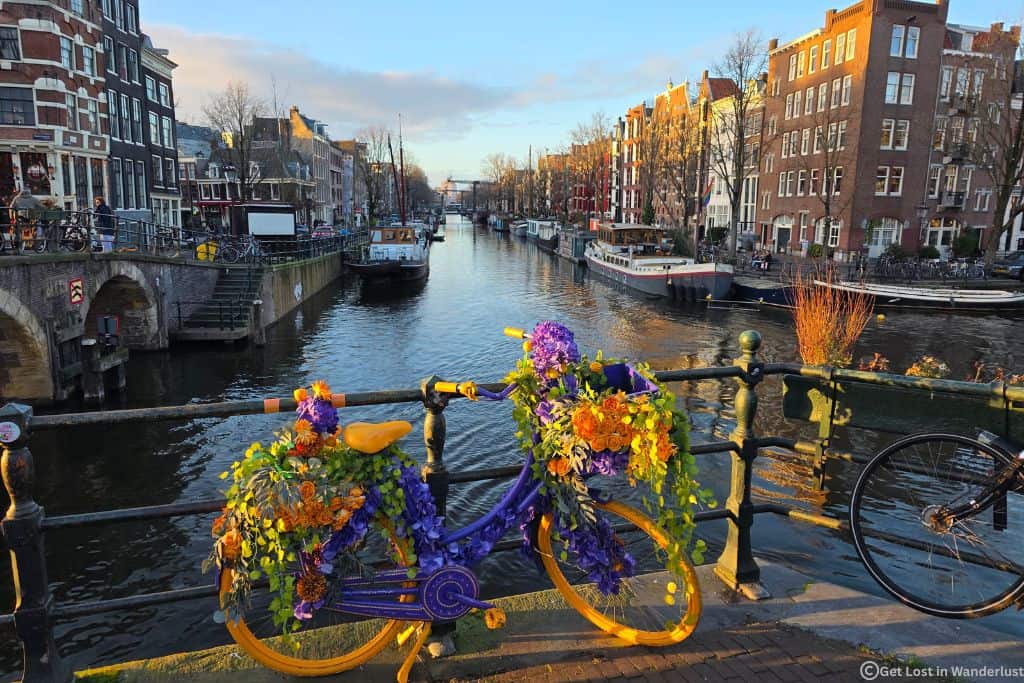 Amsterdam on a sunny day in January with a bike covered in flowers and the canals in the background.