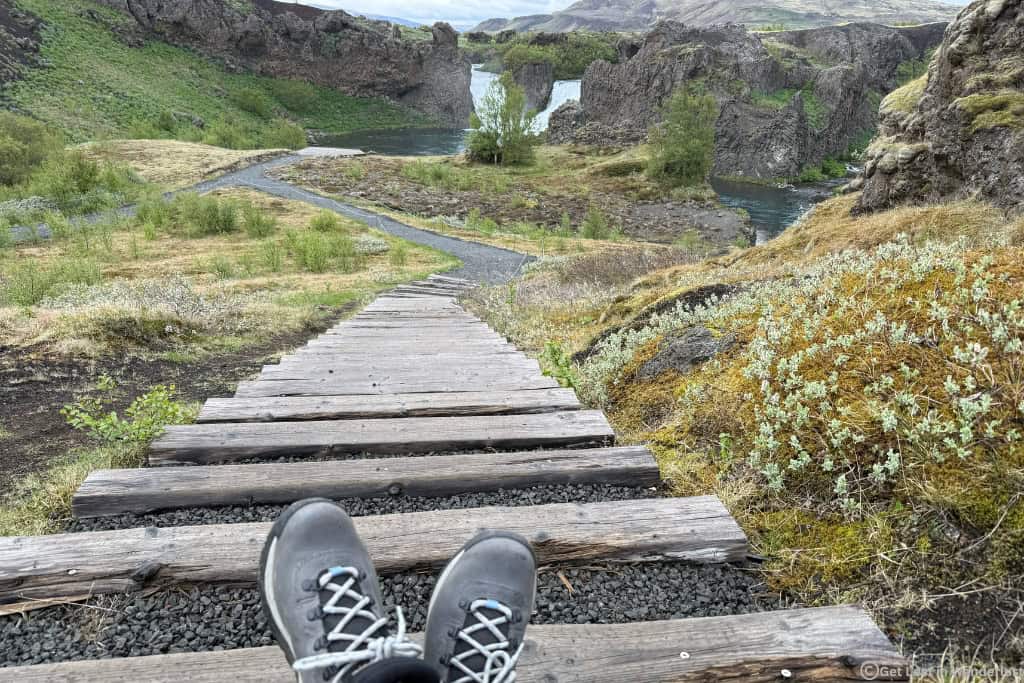 Hiking boots in front of a trail leading to a waterfall in Iceland.