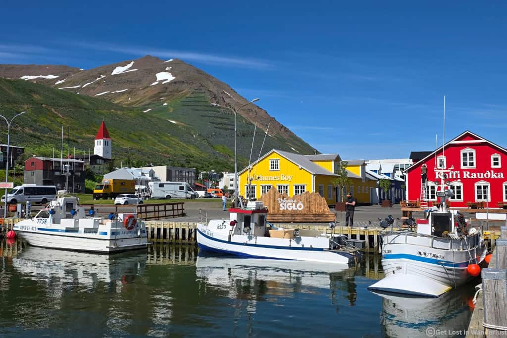Colorful harbor in Siglufjörður on Iceland's Tröllaskagi Peninsula, surrounded by mountains and fishing boats.