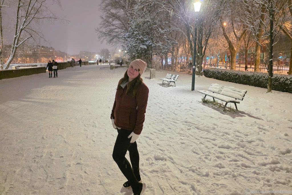 Amber (me) walking in the snow along the banks of the Seine in the 7th arrondissement, one of the best areas to stay in Paris at Christmas.