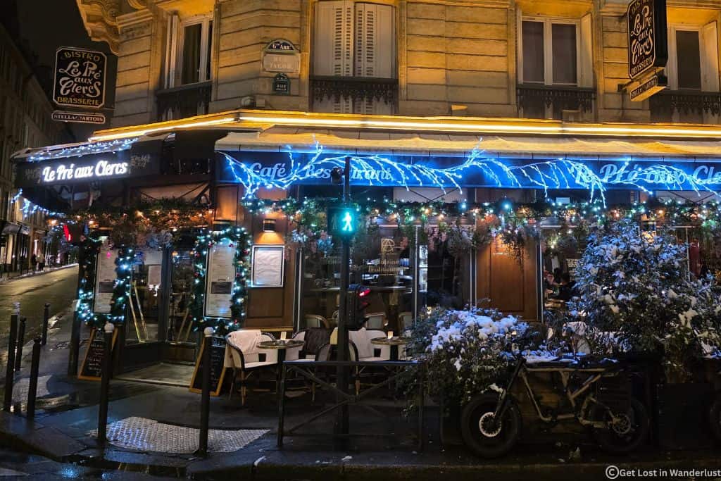 Christmas-decorated bistro in Saint-Germain, Paris, with holiday lights and snow-covered greenery