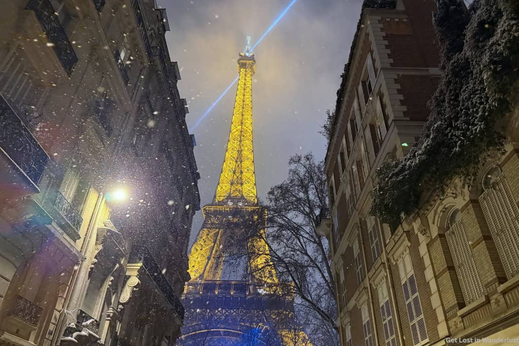 The Eiffel Tower lit up at night with snow falling, in the 7th arrondissement. If you are looking for where to stay in Paris at Christmas, this is a perfect area.