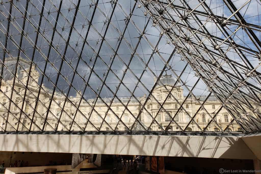 View from inside the Louvre Pyramid looking through the glass panels toward the historic Louvre Palace in Paris.