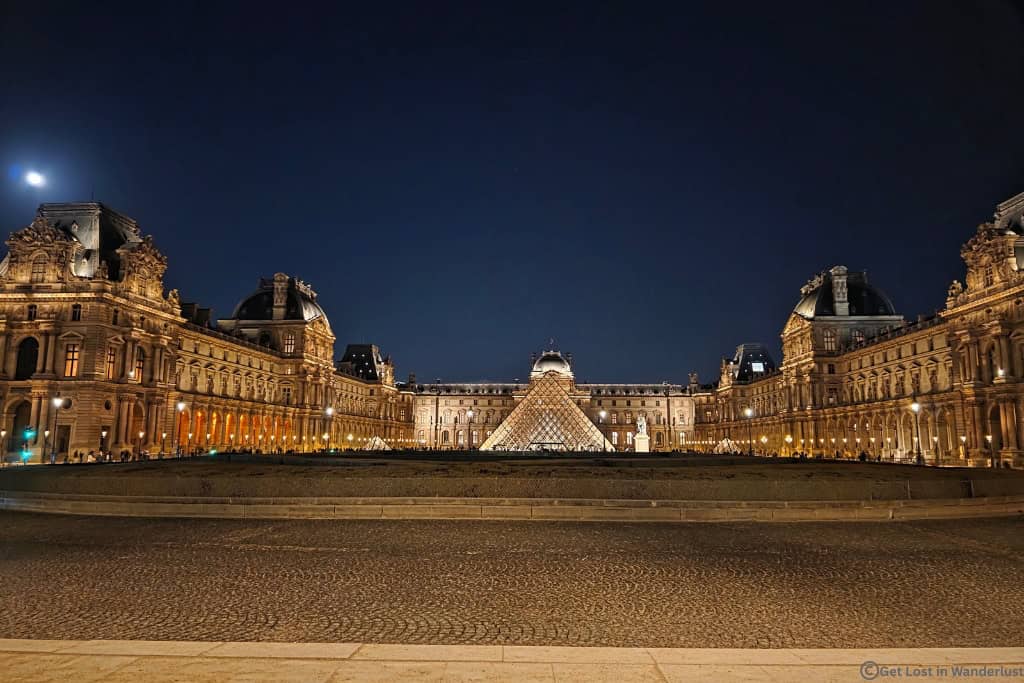 Louvre Museum and glass pyramid illuminated at night in Paris.