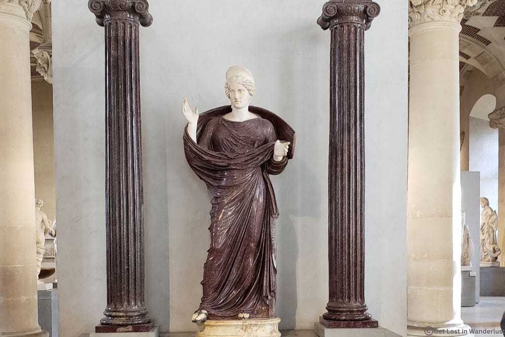 Praying Woman (Orante) Roman sculpture displayed between marble columns inside the Louvre Museum in Paris.
