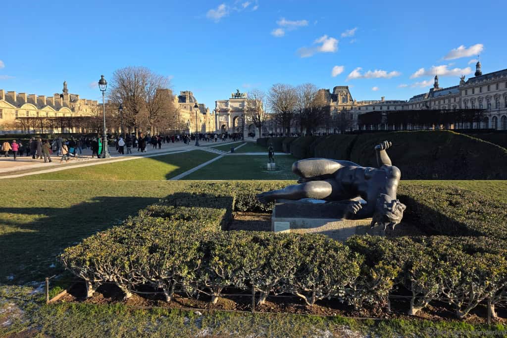 Sculpture in the Tuileries Garden with the Arc de Triomphe du Carrousel and Louvre Museum in the background.