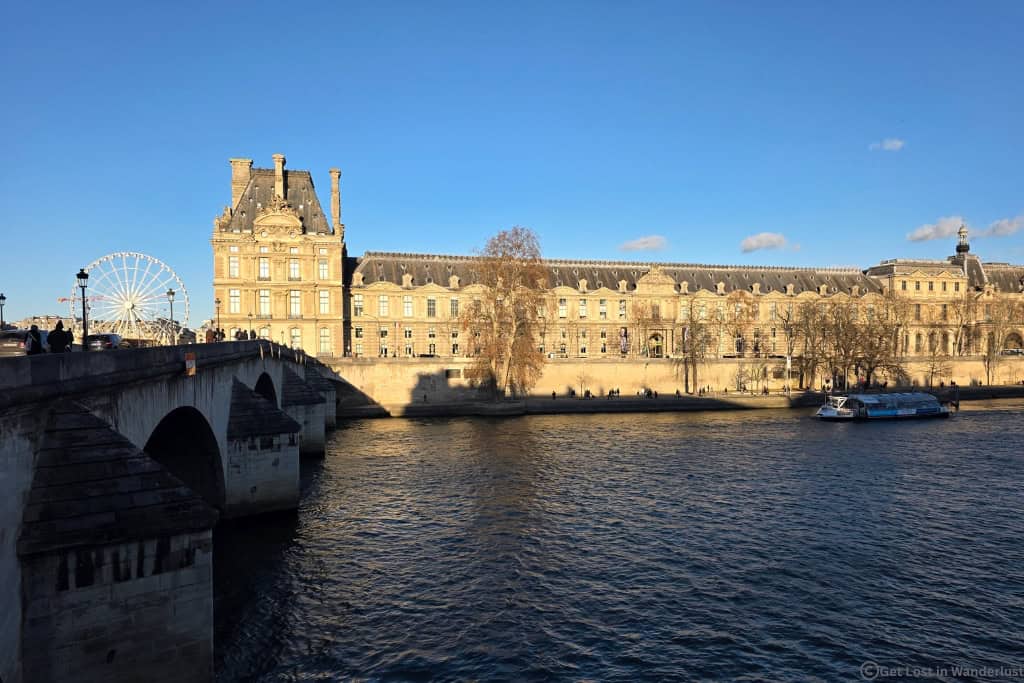 View of the Louvre Museum from the Seine River, with Pont Royal and a sightseeing boat in Paris.