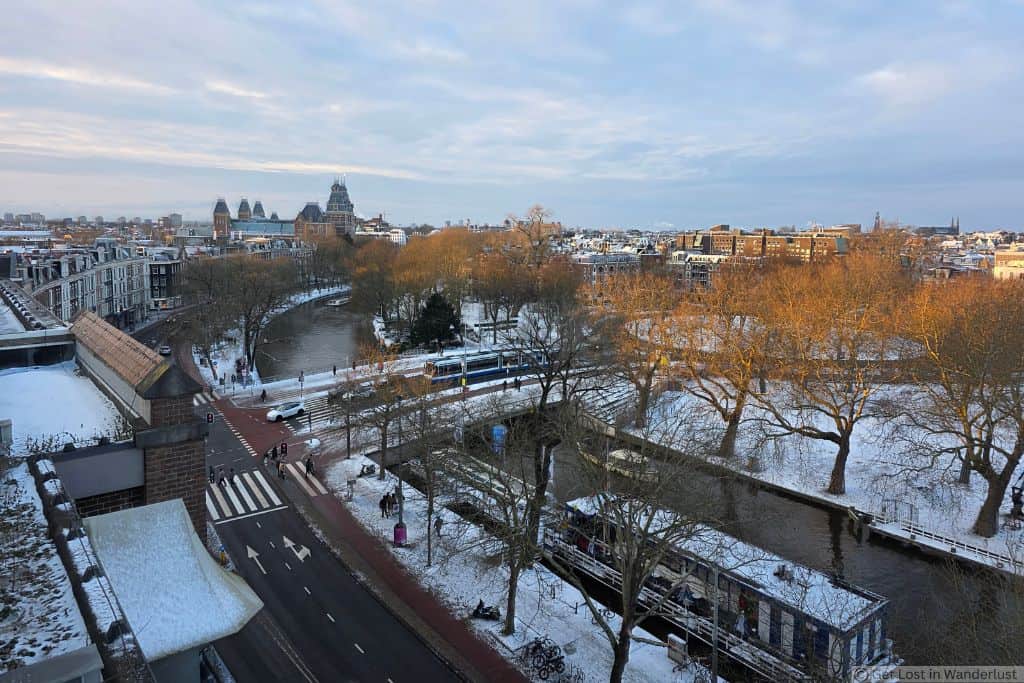 Rooftop view over Amsterdam near De Pijp neighborhood, with canals, streets, trees, and the Rijksmuseum visible in the distance. This is another neighborhood that is one of the safest places to stay in Amsterdam.