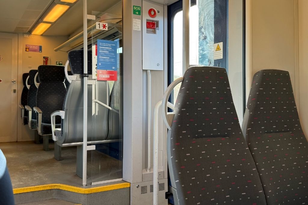 Interior of a Belgian train with rows of passenger seats and the entrance area between train cars.