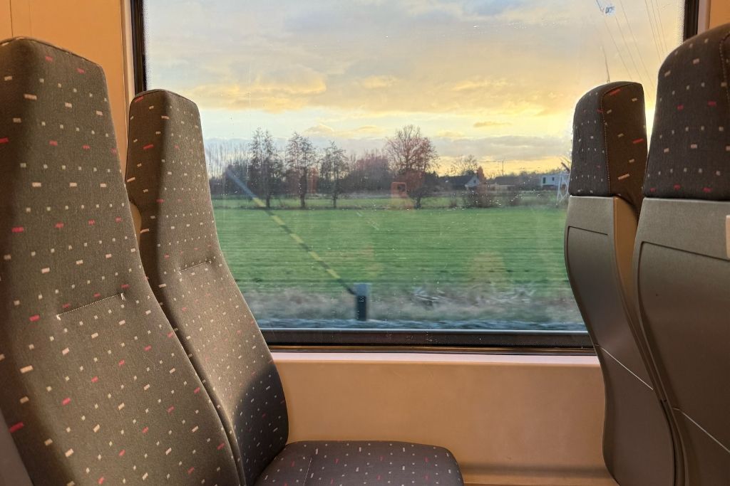 Interior of a train to Bruges, Belgium with passenger seats and a sunset view of the Belgian countryside through the window.