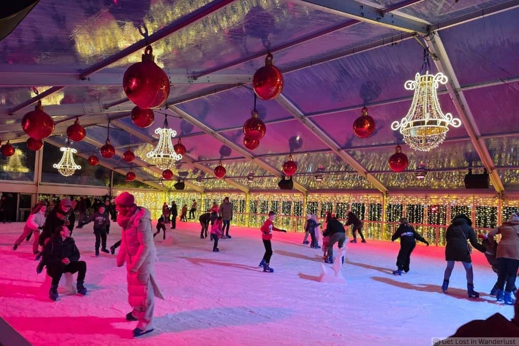 Ice skating rink at Bruges Winter Glow Festival decorated with red ornaments, chandeliers, and festive Christmas lights.