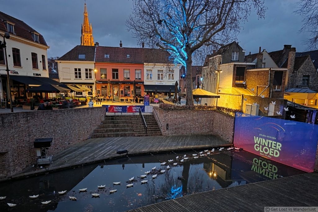 Bruges Winter Glow Festival at dusk with illuminated trees, light installations, and reflections along a canal in the historic city center.