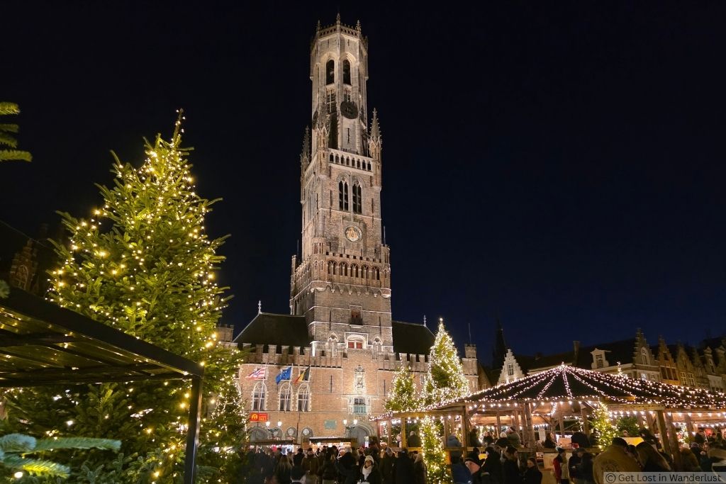 Bruges Christmas Market at night with illuminated Christmas trees and the Belfry of Bruges in Markt Square.