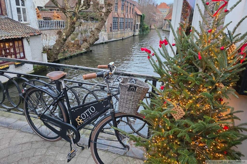 Bicycle beside a decorated Christmas tree overlooking a canal and historic buildings in Bruges, Belgium.
