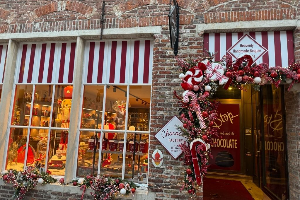 Belgian chocolate shop in Bruges decorated for Christmas with red-and-white candy cane garlands, ornaments, and festive window displays.