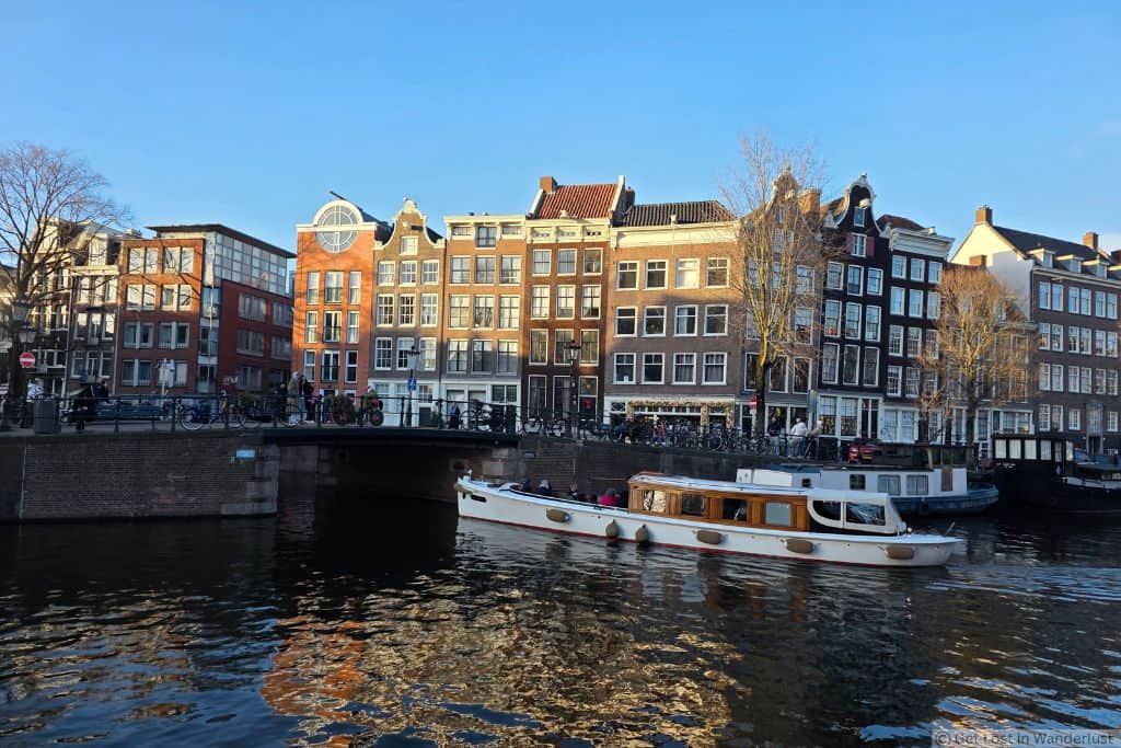 Canal boat passing historic canal houses in Amsterdam’s Jordaan neighborhood on a clear winter day. One of the top areas and safest places to stay in Amsterdam.