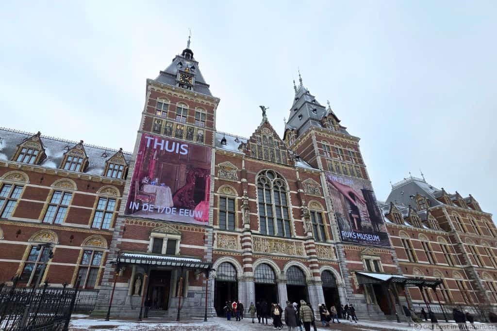 Rijksmuseum in Amsterdam’s Museum Quarter on a snowy winter day, with visitors gathered outside the historic museum entrance.